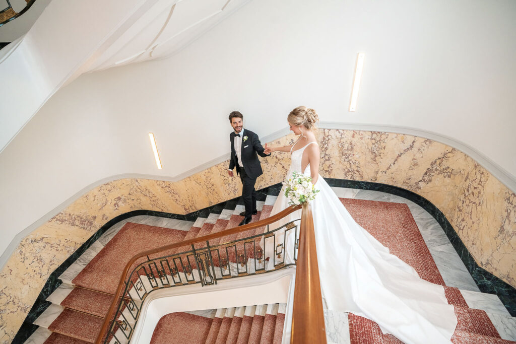 Hochzeitspaar geht zusammen die wunderschöne Treppe hinunter im Madarin Oriental Palace Luzern